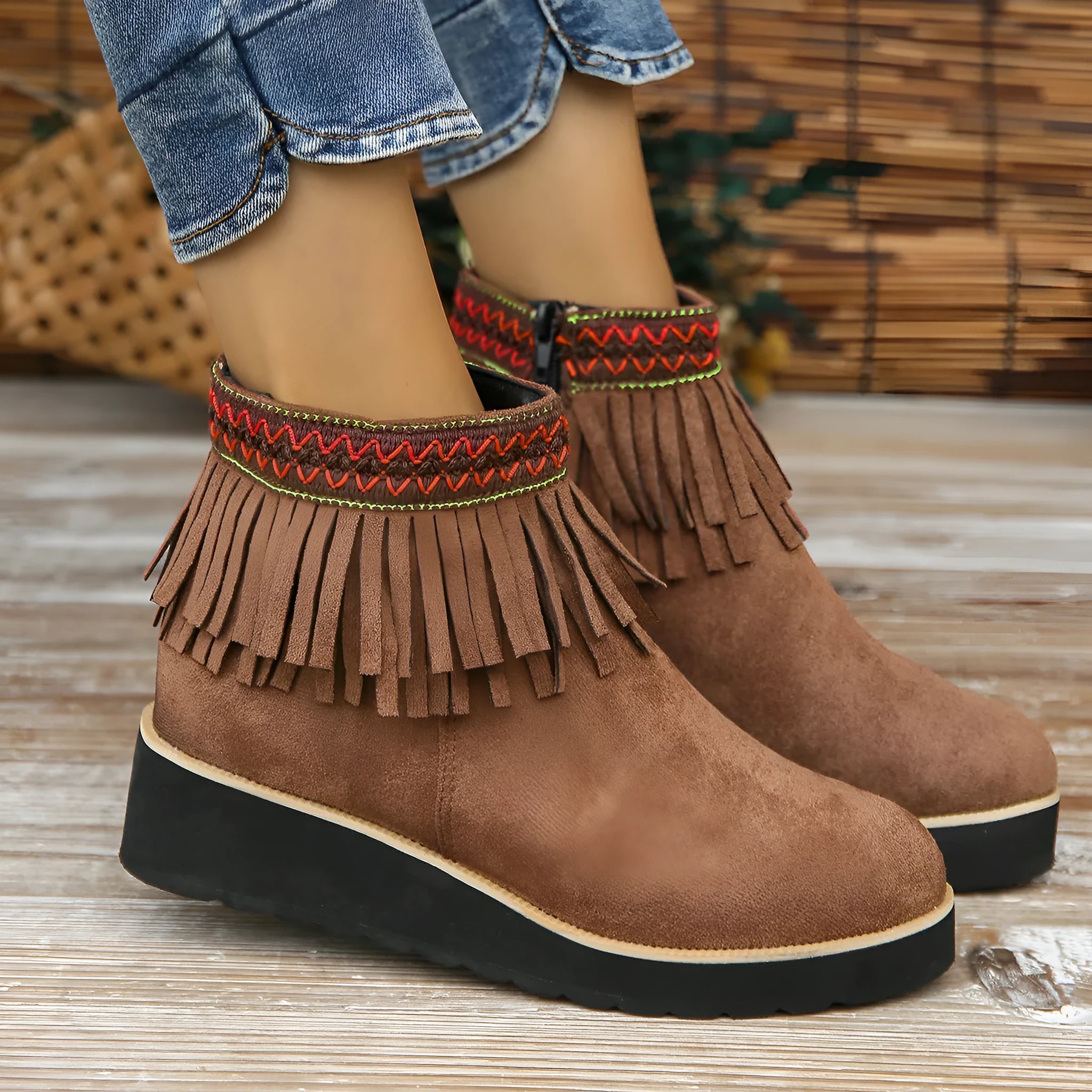 Women's ankle boot in suede with wedge heel, side zipper, and tassel detail on a dark background.