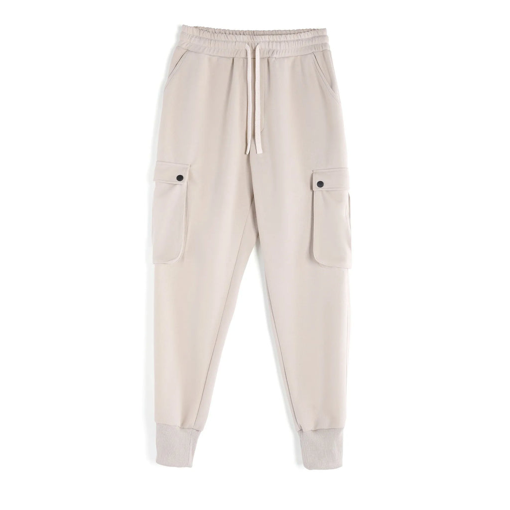 Men's loose fit beige cotton trousers with an ankle tie and multiple pockets on a man standing casually.