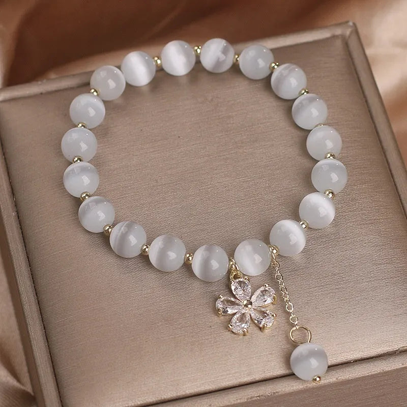 Close-up of a white cat's eye crystal bracelet with a flower tassel pendant and a morganite safety buckle.