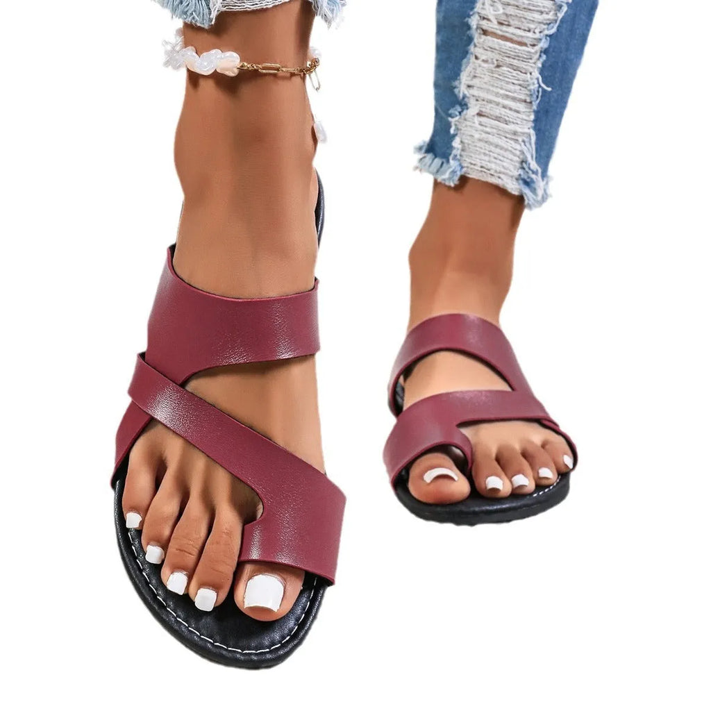 Simple solid colour beach slippers with round head, one-line design and hollow-out details on a sandy background.