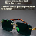 Dark green frameless crystal sunglasses with a distinctive design, shown with a hard case and lens cloth.