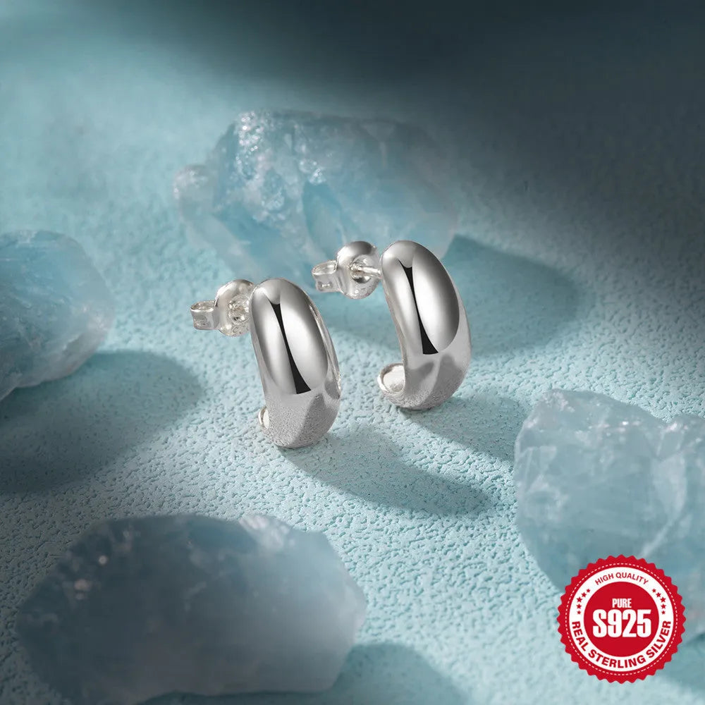 Glossy gold and silver tone C-shaped sterling silver stud earrings on a plain background.