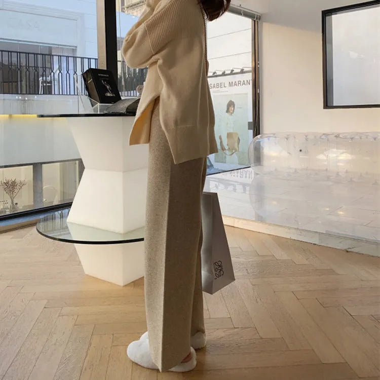 Woman wearing cream white high-waisted knitted wide-leg pants with a drooping mopping silhouette.